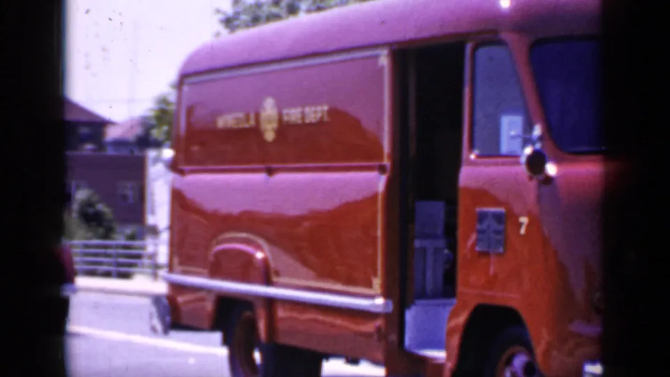 The Mineola Fire Dept. van passes close to camera, with side lettering, cab window, and red bodywork prominent.