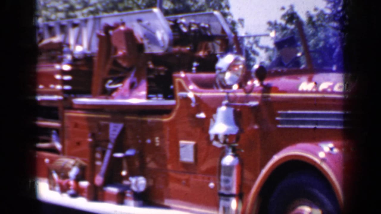 Close side view of a red Mineola fire truck with open cab, chrome fixtures, and ladder rack.