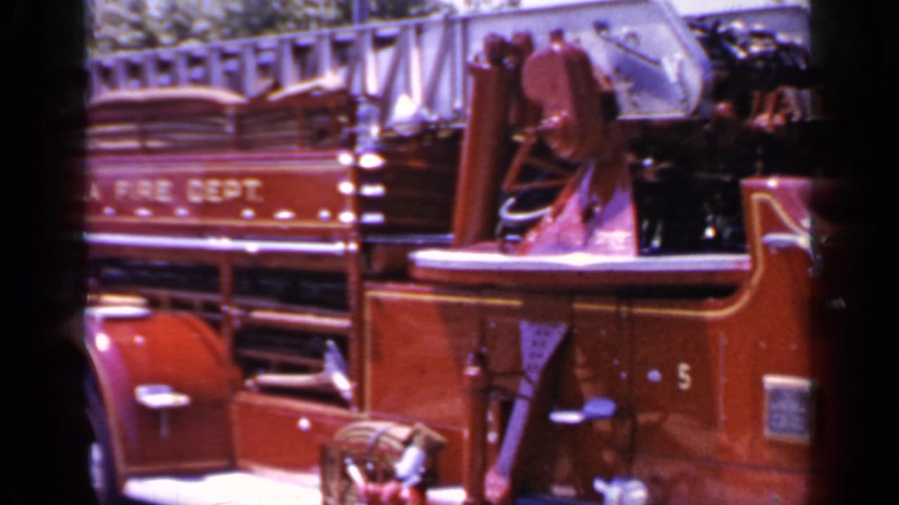 Red fire truck side with open cab, ladder rack, chrome bell, and Mineola Fire Dept. lettering.