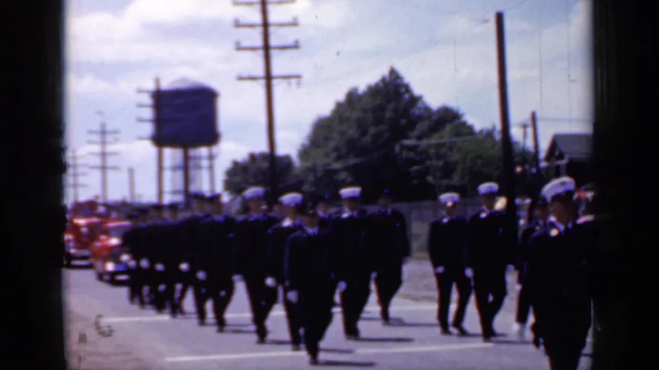 Dark-uniformed marchers, likely firefighters with naval-style caps, walk in formation during the 1966 Mineola parade.