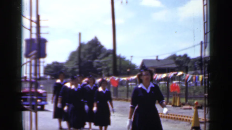 Women in matching dark dresses with white collars, likely nurses, march in the 1966 Mineola street parade behind the uniformed group.