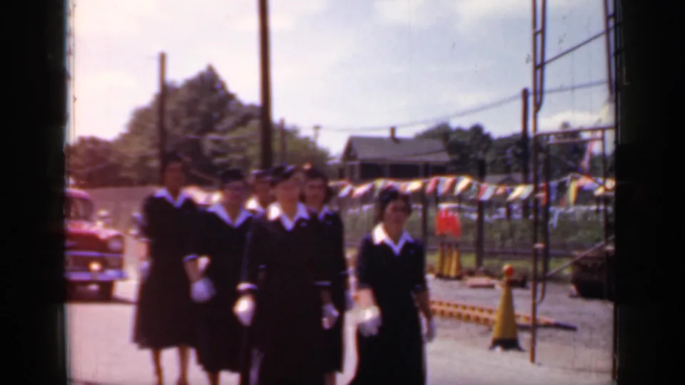 A small group of uniformed women passes close to the camera during the 1966 Mineola outdoor procession, with roadside details behind them.