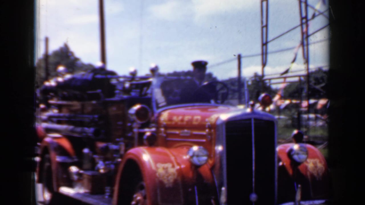 Red vintage fire truck approaching with chrome grille and bell visible.