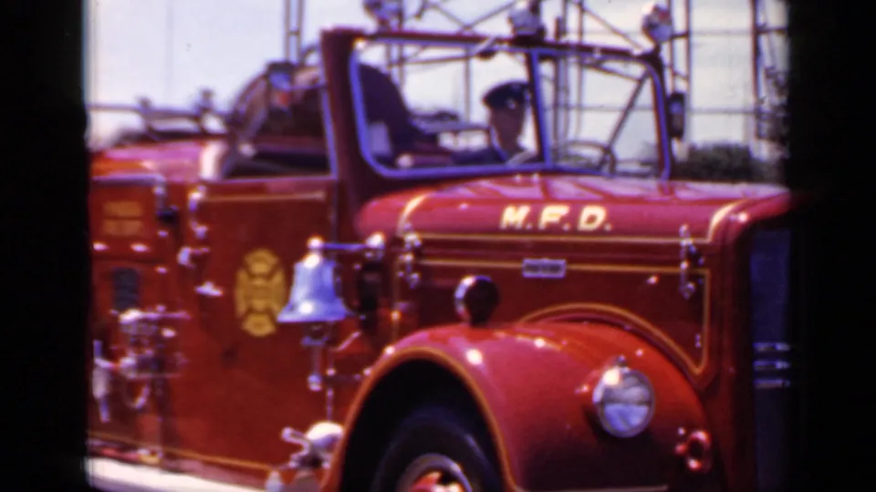 Mineola 1966 parade frame showing the red M.F.D. truck cab, driver in dark uniform hat, bell, insignia, and gold trim.