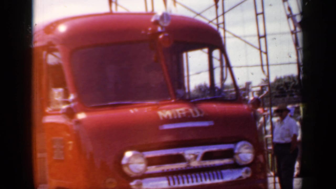 Front of a red fire truck with round headlights and a person standing nearby.