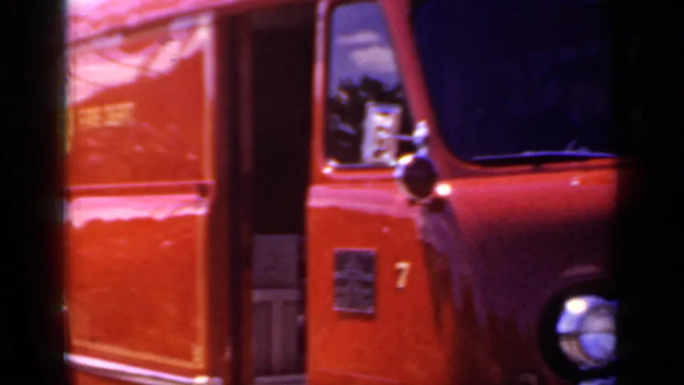 Side view of the red Mineola fire truck showing the door, front corner, headlight, and dark window in soft 8mm motion blur.