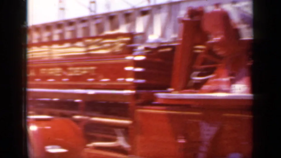 A red fire truck moves through a 1966 Mineola, New York parade, partly blurred by the close handheld 8mm camera position.