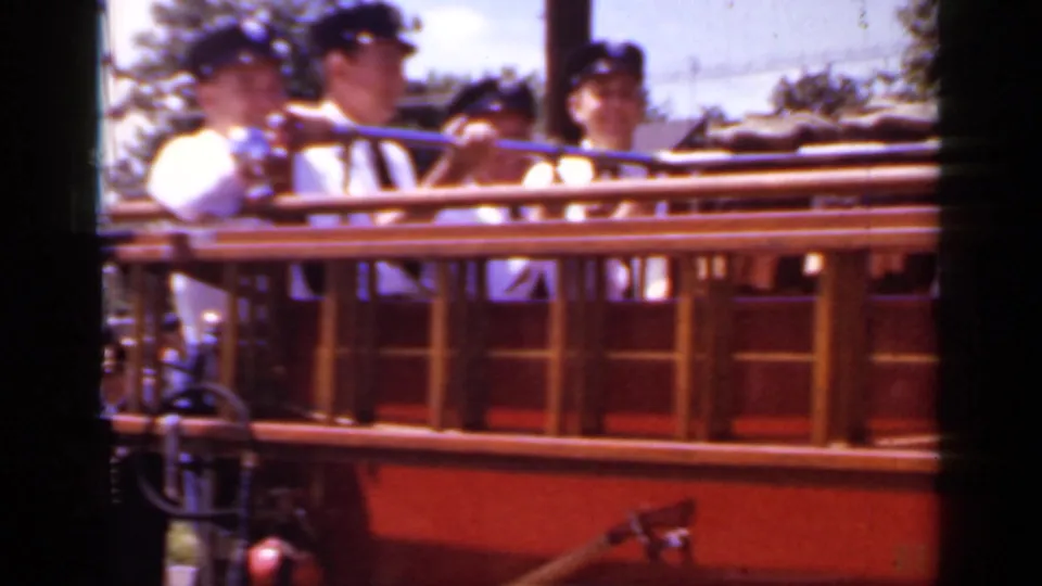 Three firefighters in white dress uniforms and dark caps ride behind the rail of the red fire truck in the 1966 Mineola parade.