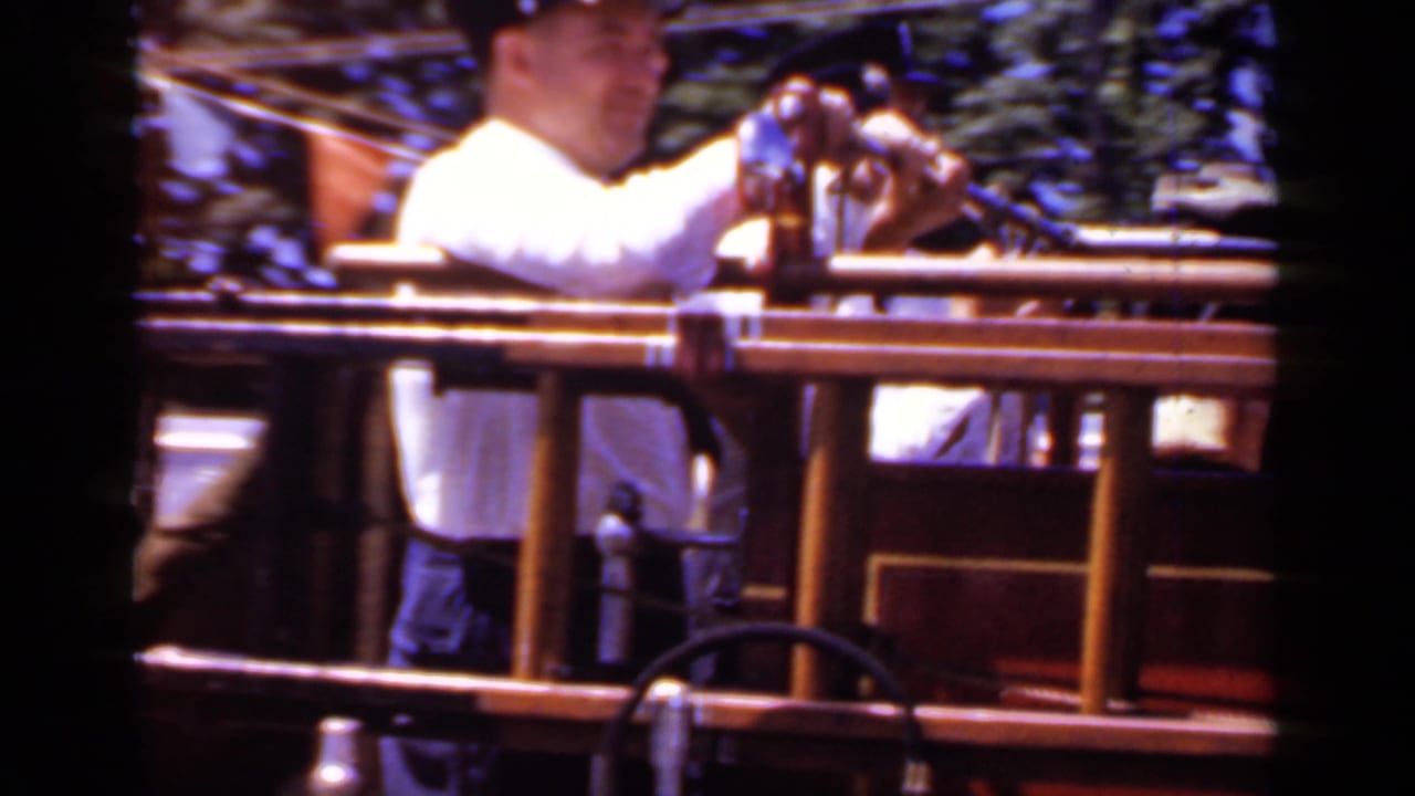 A firefighter stands beside the rail of a red parade rescue vehicle.