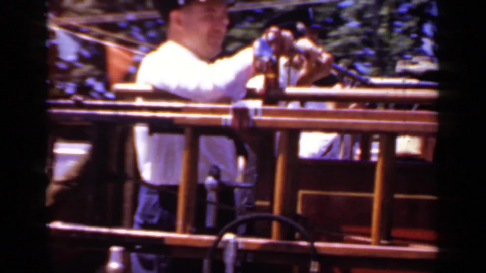 A uniformed firefighter on the 1966 Mineola parade vehicle is seen near chrome rails and red bodywork.