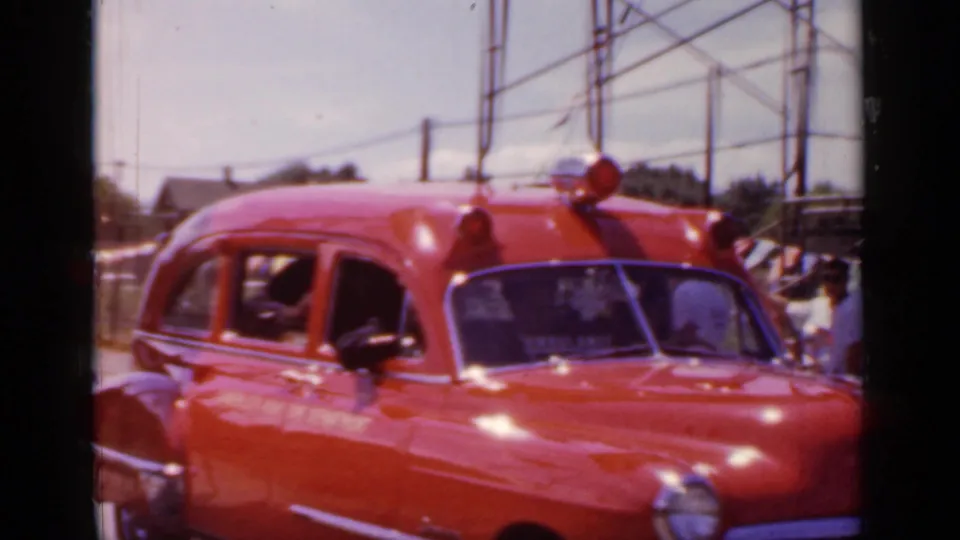 Red 1950s-style ambulance in Mineola, New York, seen from the front side as it passes in 1966 home-movie footage.