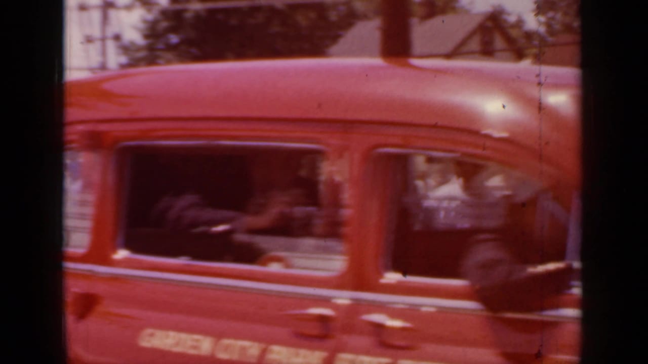 Close side view of the red Garden City Fire Department ambulance passing through Mineola in 1966 footage.