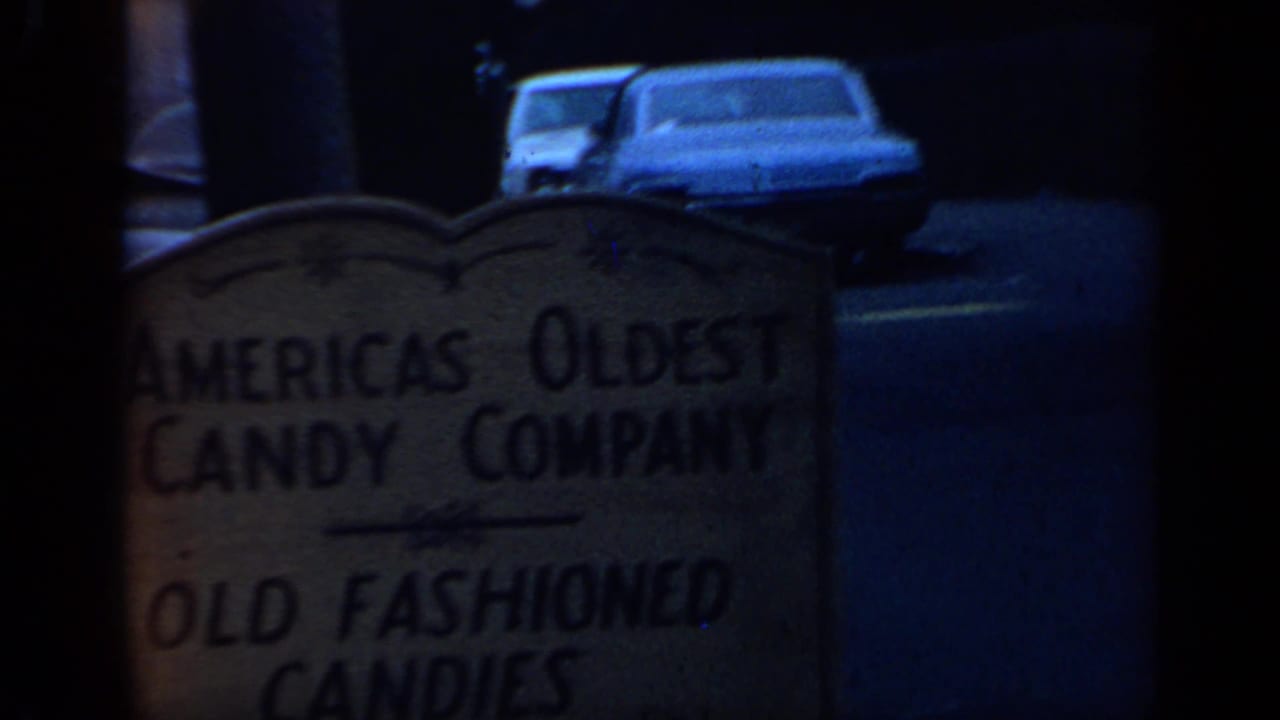 Weathered candy-company sign seen through dark 8mm framing with parked cars behind it.