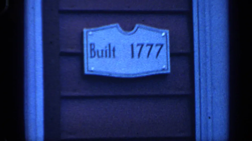Blue-tinted 8mm view of a "Built 1777" plaque mounted on wooden siding in Massachusetts footage from 1968.