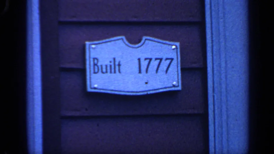 Later 8mm frame holds on the "Built 1777" plaque and adjacent trim, with strong blue color shift and soft focus.