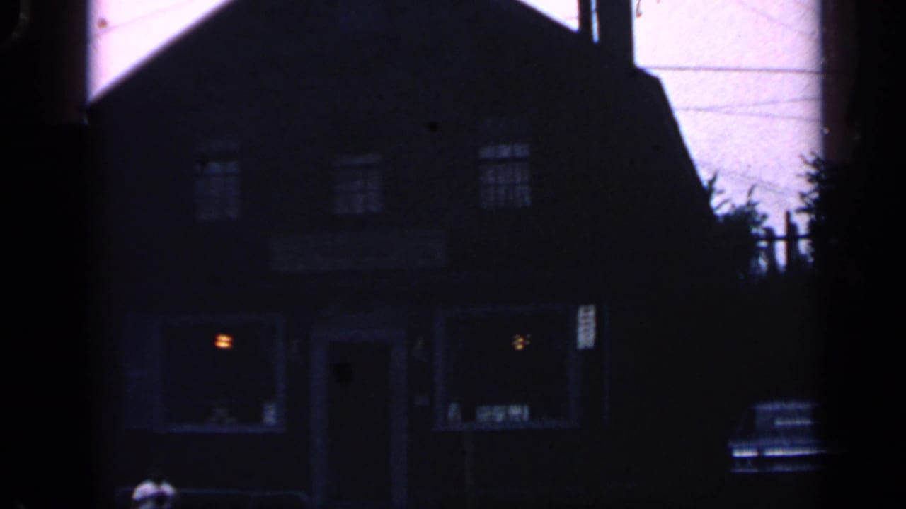 Low-angle dark exterior of a two-story building with glowing windows and a parked car.