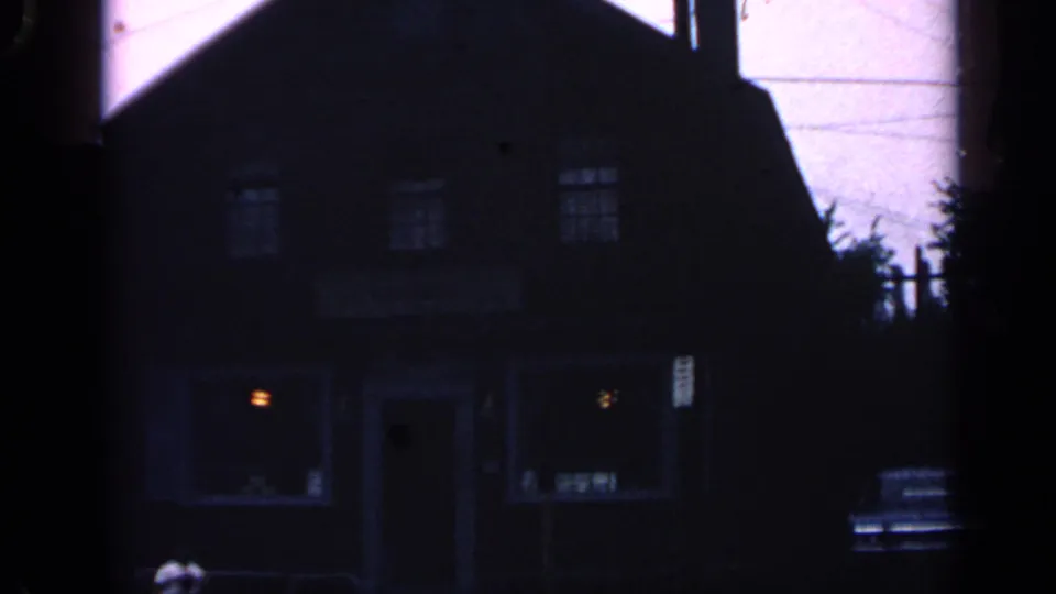 Low-angle 1968 Massachusetts home-movie view of a dark historic-looking building with lit windows and a car at the curb.