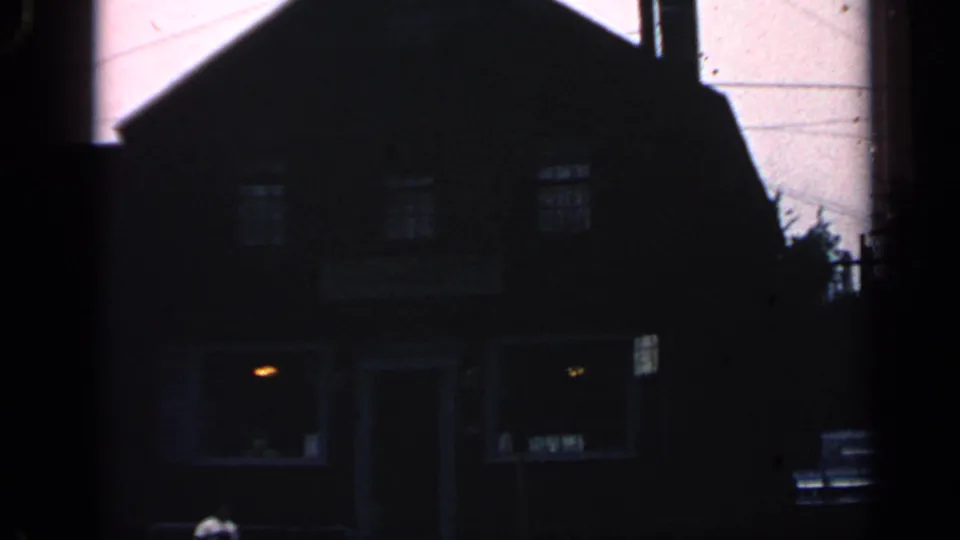 1968 Massachusetts 8mm exterior of the dark building, with warm window light and a faint passerby near the entrance area.