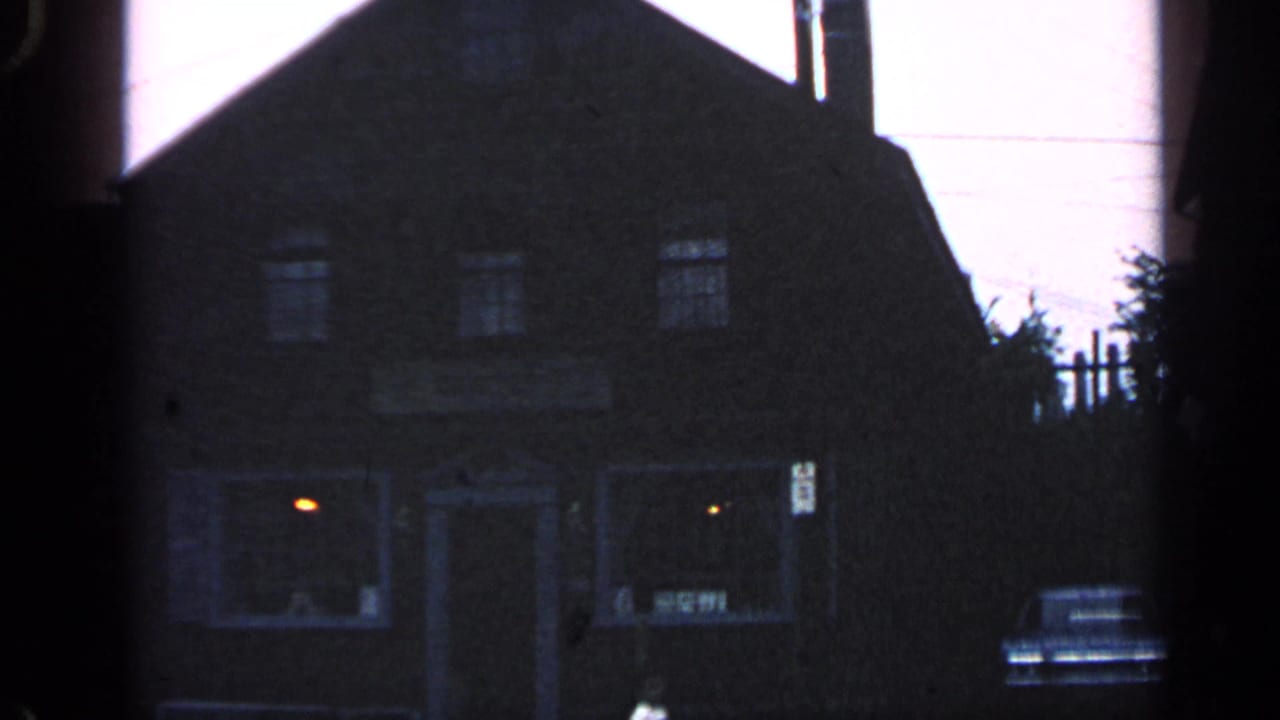 Dark gabled building at dusk with porch windows and a parked car near the entrance.