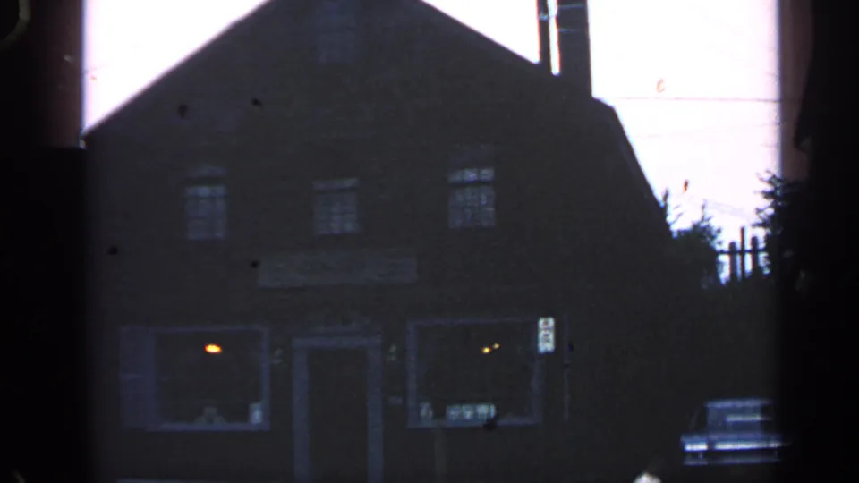 1968 Massachusetts home-movie frame of a dim historic-looking building exterior during a visitor zoom.