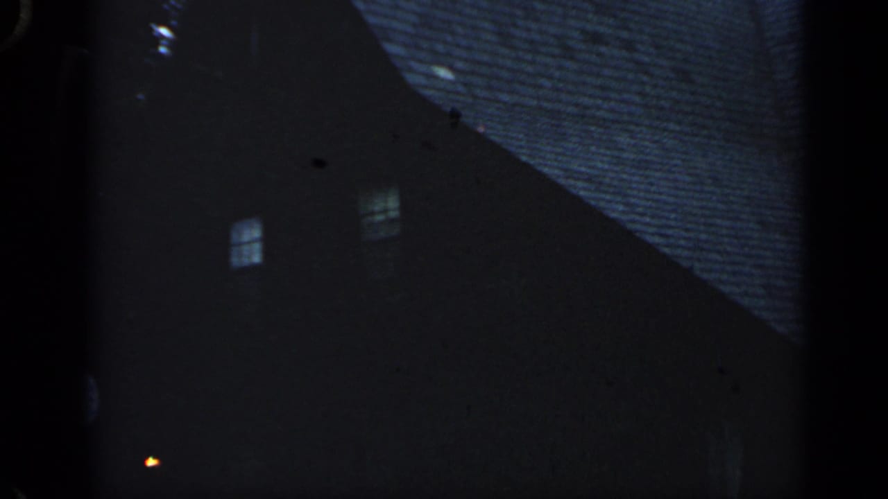 Dark two-story house exterior with lit windows and a small light near the lower left.