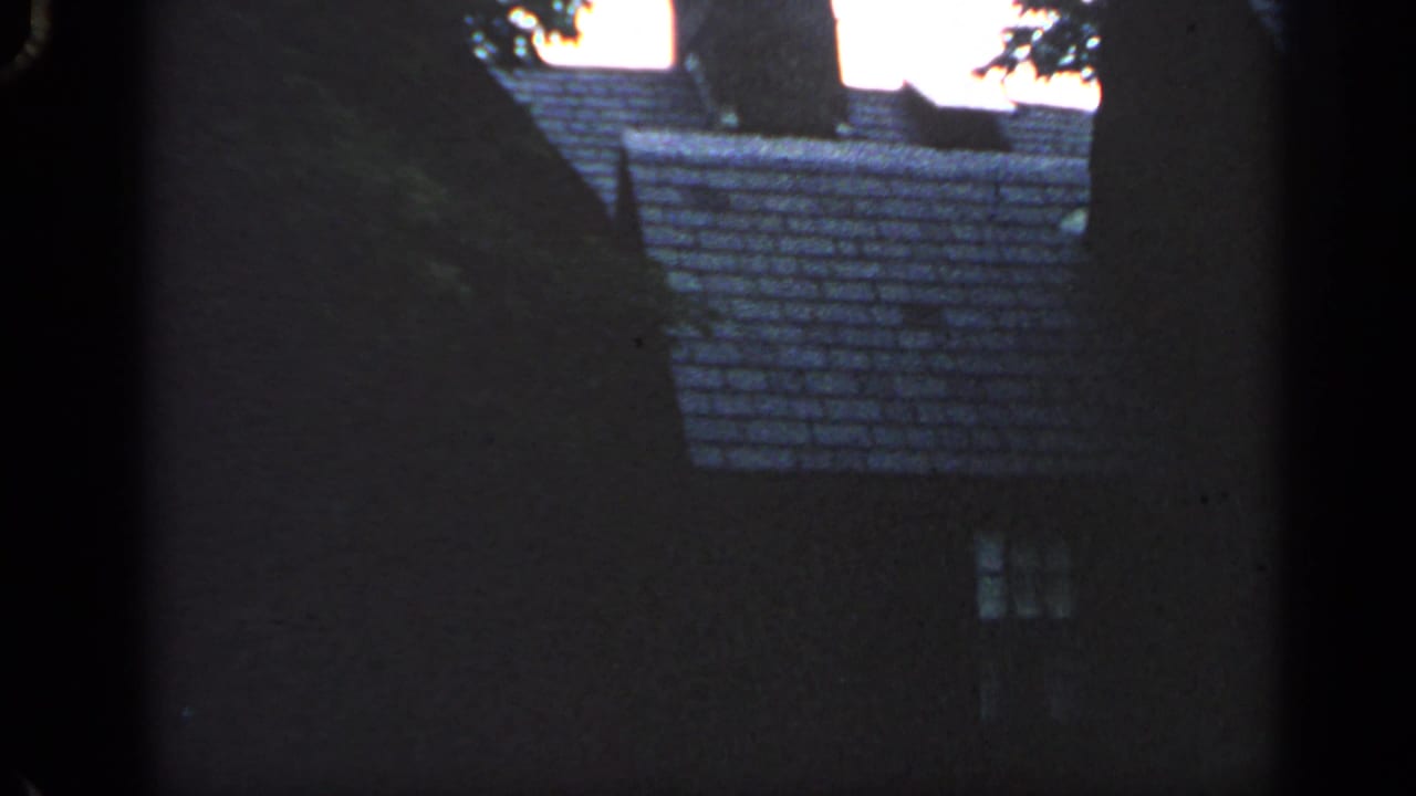 Dark residential house roof and small window partly framed by trees and film gate edges.