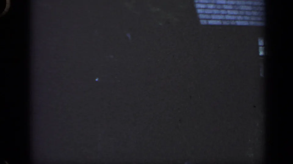 Low-exposure 1968 Massachusetts 8mm frame showing part of a house, roof edge, small window, trees, and a shadowed yard area.