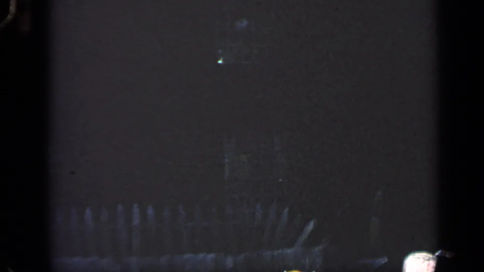 Final 1968 Massachusetts 8mm frame revealing a dim yard, faint fence line, partial house exterior, small window, and surrounding trees.