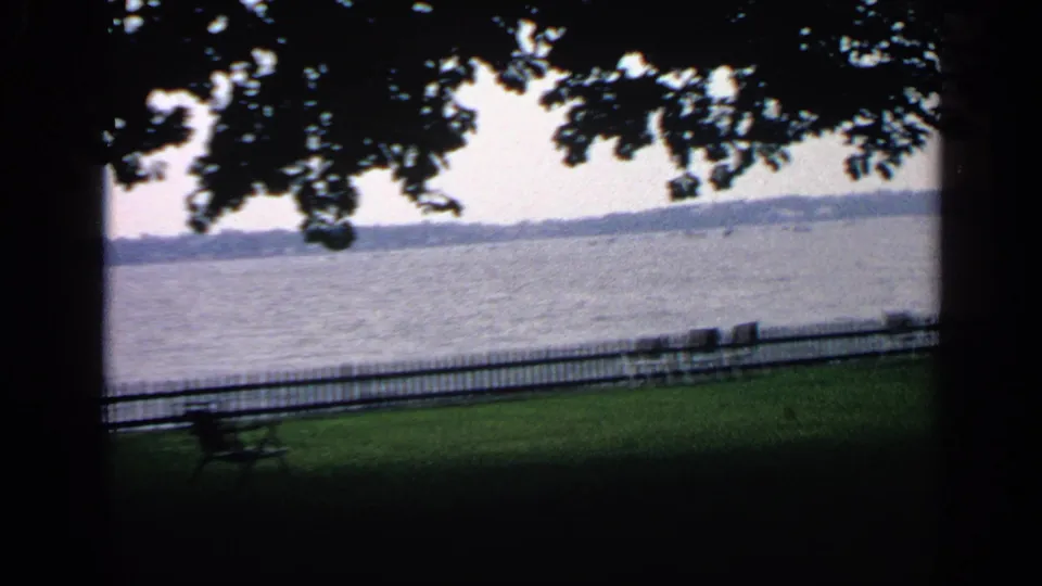 1968 Massachusetts frame of a quiet waterfront park, with benches and a fence in the foreground and lake water beyond.