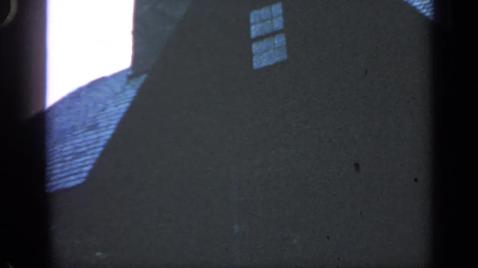 1968 Massachusetts frame showing part of a nearby building wall, roofline, window, and deep shadow beside the park view.