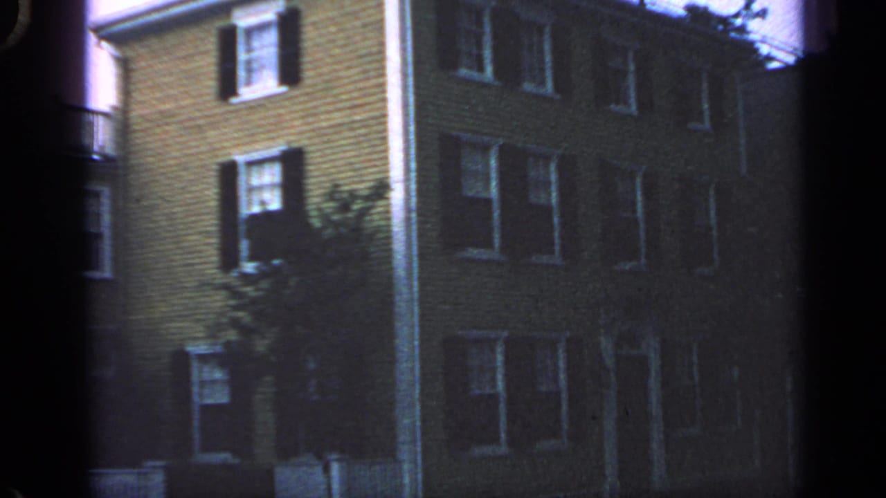 Multi-story residential building with dark shutters, white trim, and a tree at the side.