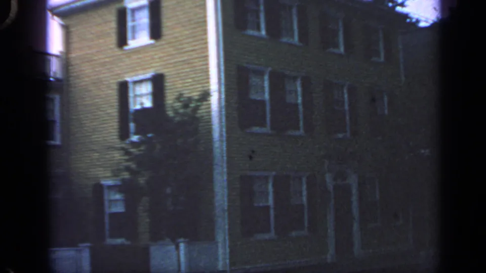 1968 Massachusetts 8mm still showing a residential building facade, dark shutters, white-trimmed windows, and tree branches.