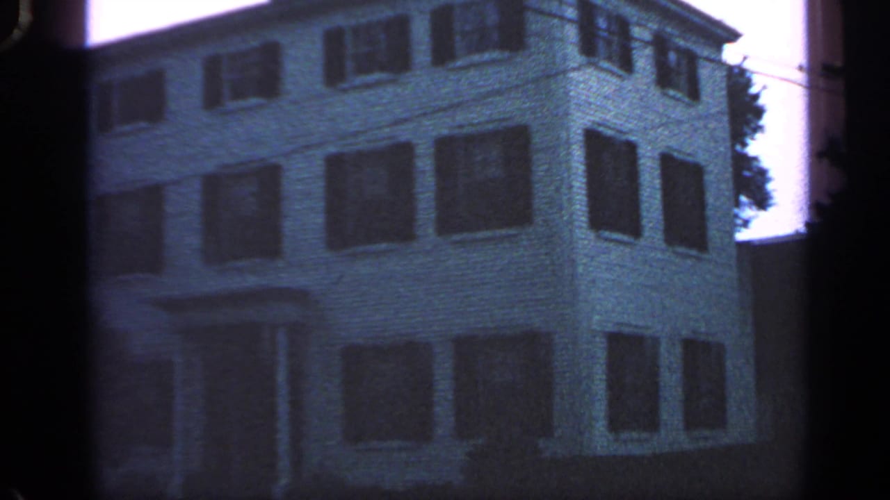 White multi-story building with dark shutters, seen through a soft 8mm frame.