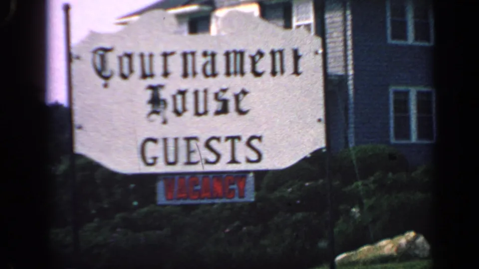 1968 Massachusetts 8mm frame showing a Tournament House guests sign with a red vacancy notice, shrubs, and clapboard building behind it.