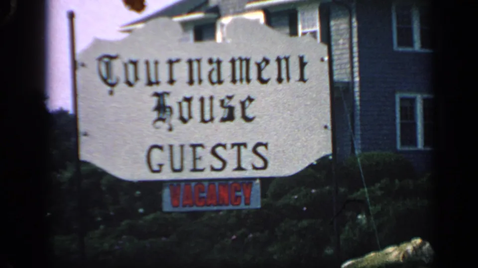 1968 Massachusetts home-movie frame centered on the Tournament House sign, red vacancy notice, shrubs, and clapboard guesthouse exterior.