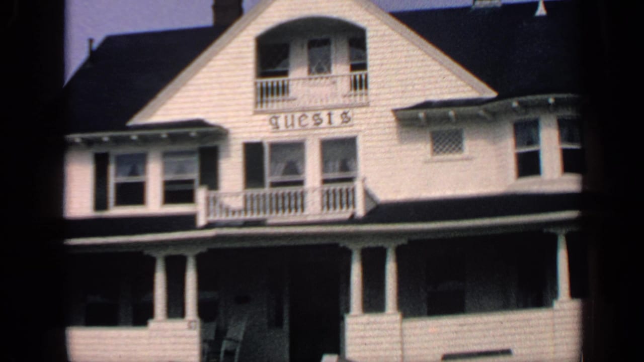 White shingled house with porch columns, balcony, front windows, and GUESTS sign.