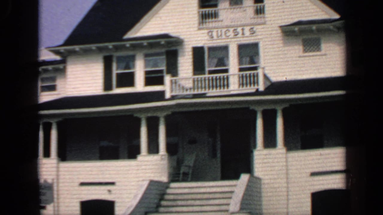 1968 Massachusetts home-movie view of a white house exterior with central steps, porch columns, balcony railing, and GUESTS sign.