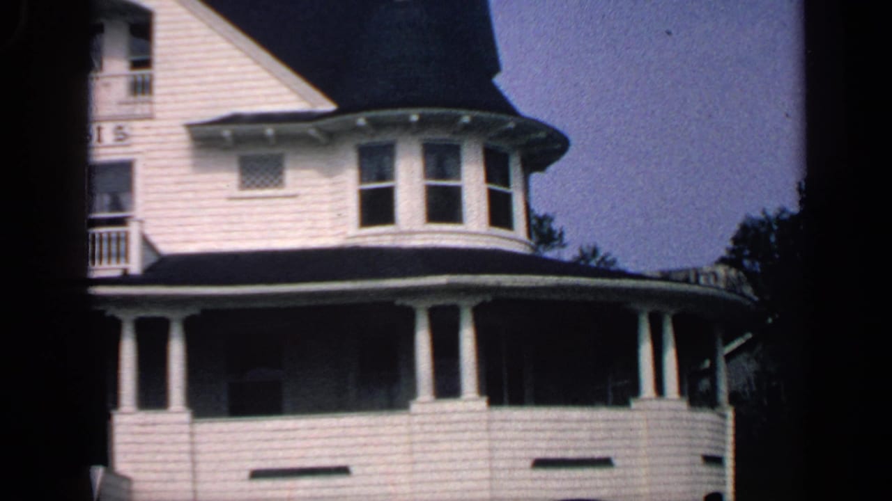 White shingled coastal house with porch columns and a rounded turret.