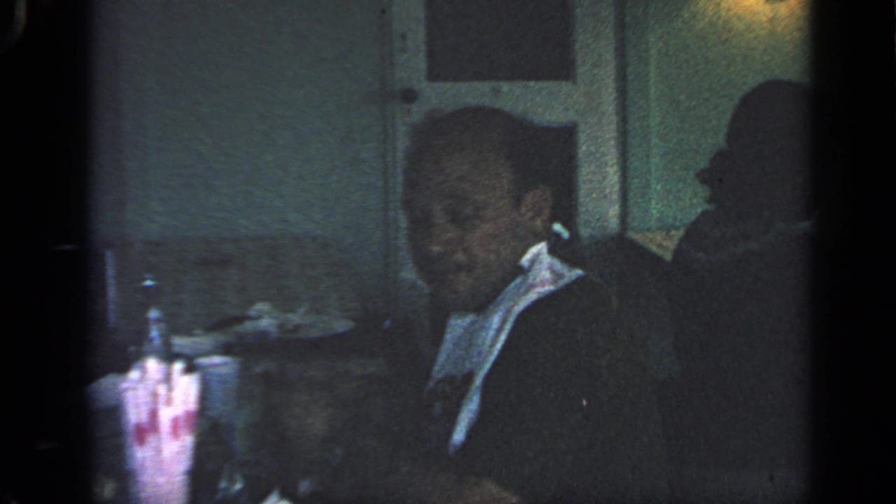 Older man in a dim restaurant wearing a white bib at a table.