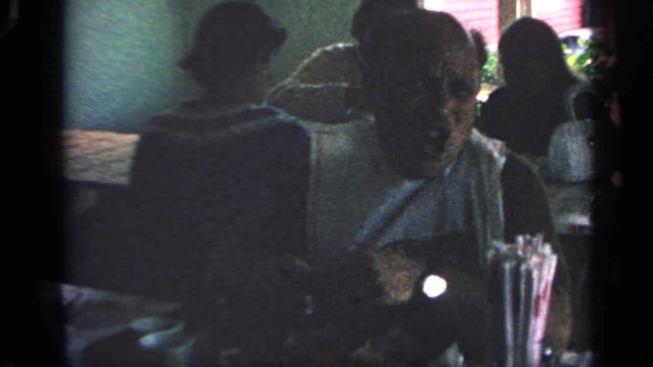 Dim restaurant scene with seated diners and table items in the foreground.