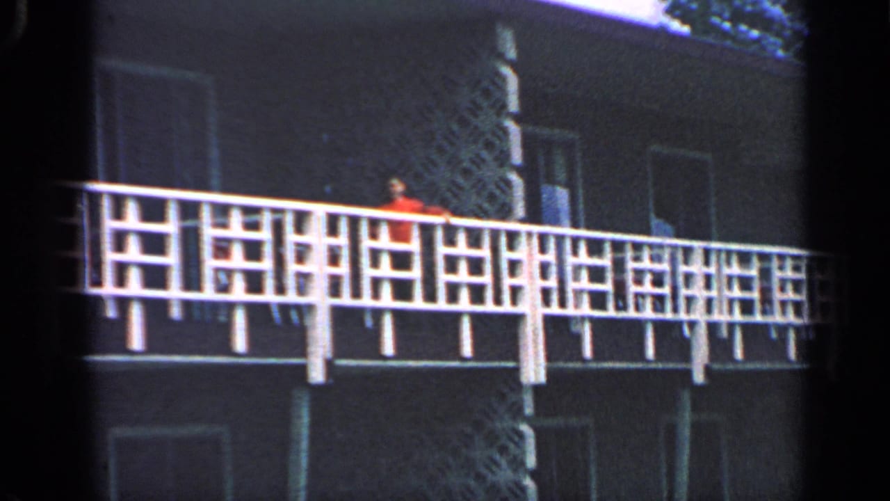 Closer view of an upper balcony railing with a person in an orange shirt near the apartment wall.