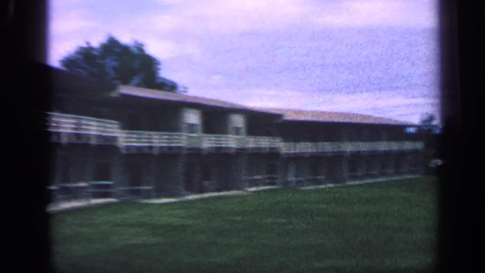 1968 Massachusetts 8mm frame showing a low-rise apartment building, white balcony railings, lawn, and overcast sky.