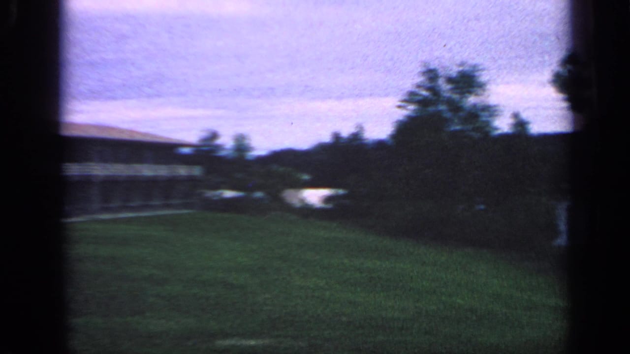 Handheld 8mm view across residential grass toward trees, shoreline, and water in Massachusetts.