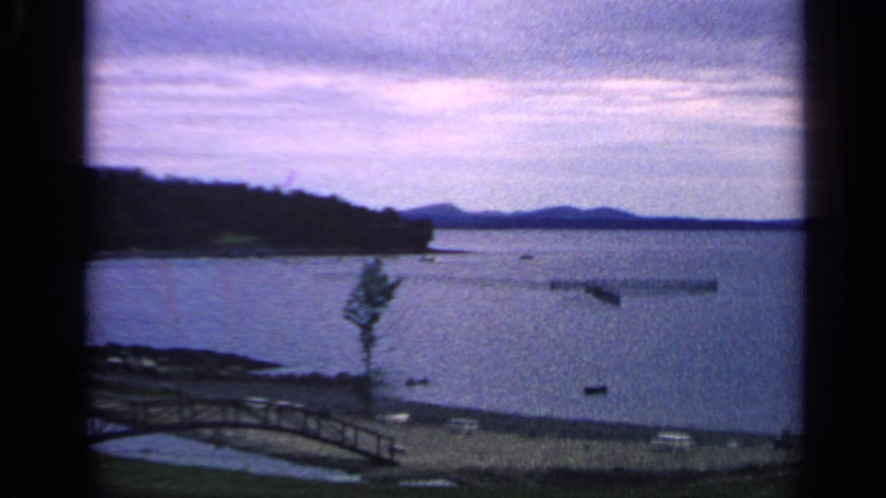 Calm lake with wooded shoreline, small bridge, boats, cloudy sky, and dark film borders.