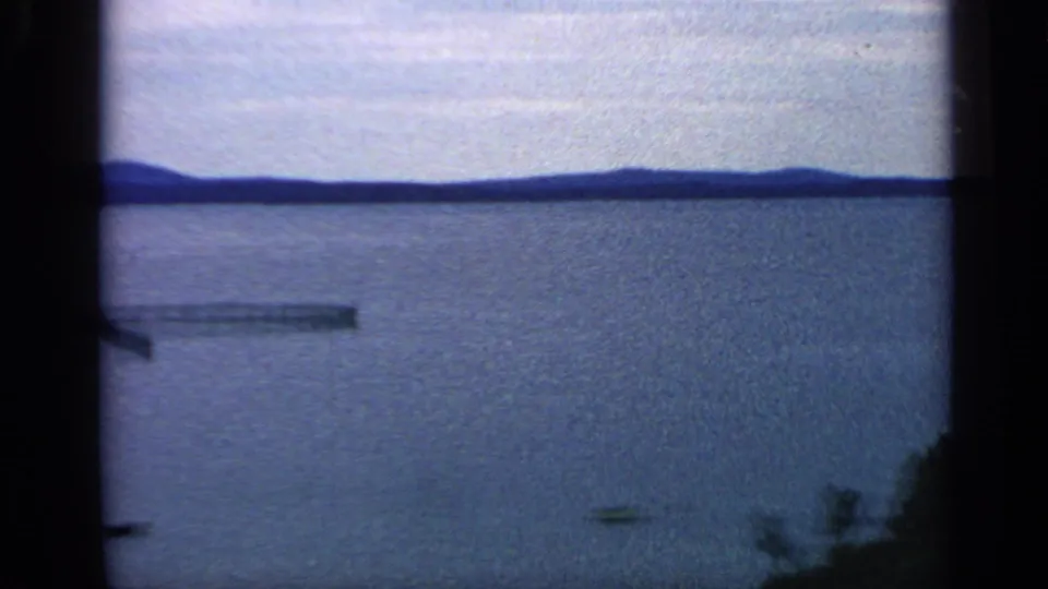 1968 Massachusetts 8mm frame with open lake water, low hills on the horizon, a small boat, and a narrow dock-like form near shore.
