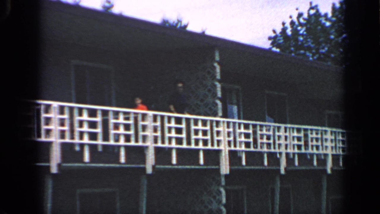 Dark building with white balcony railing and small people on the upper walkway.