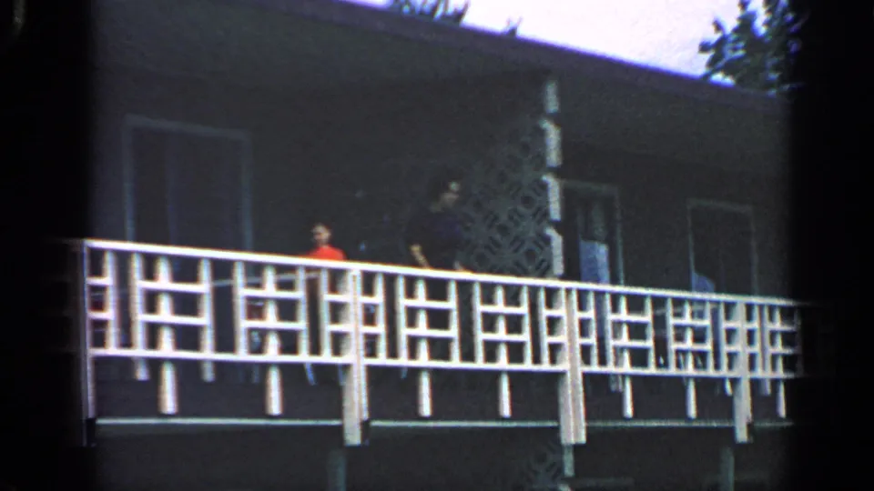 1968 Massachusetts 8mm frame with a white geometric railing across a dark building and small indistinct visitors on the balcony.