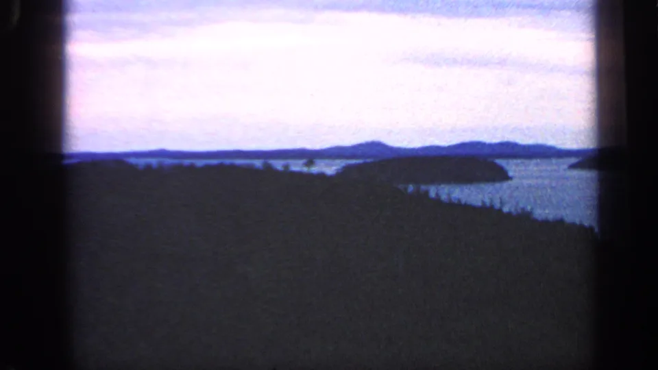 1968 Massachusetts home-movie frame showing a broad body of water, wooded shoreline, islands, and distant low hills.
