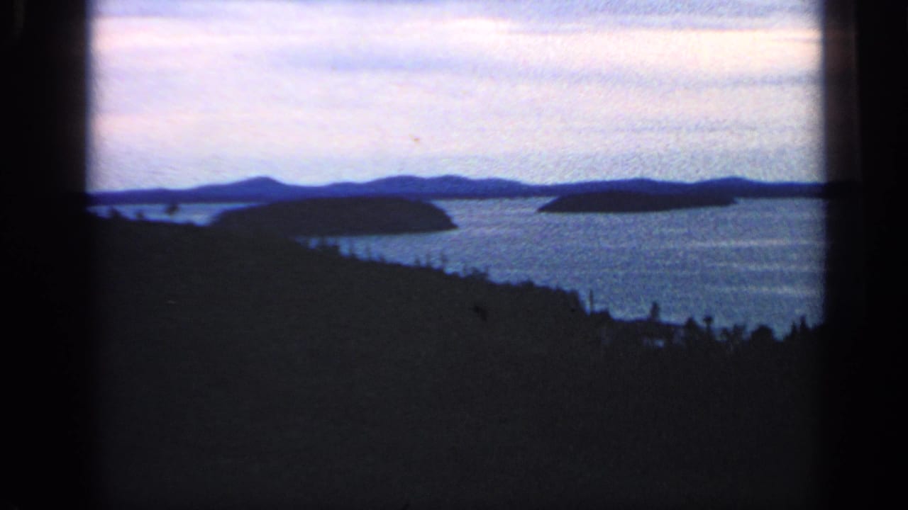 Distant islands across calm water with dark shoreline trees in the foreground.