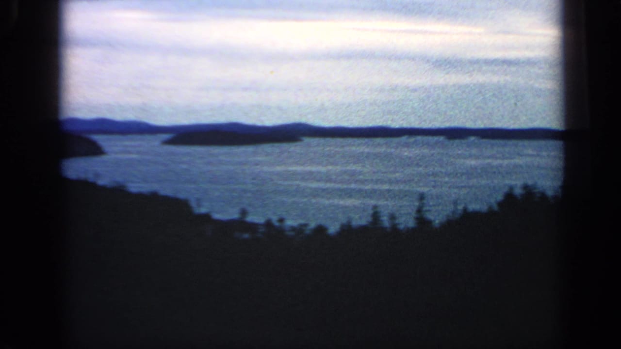 Massachusetts home-movie frame from 1968 with low islands across blue water and a silhouetted treeline below the horizon.